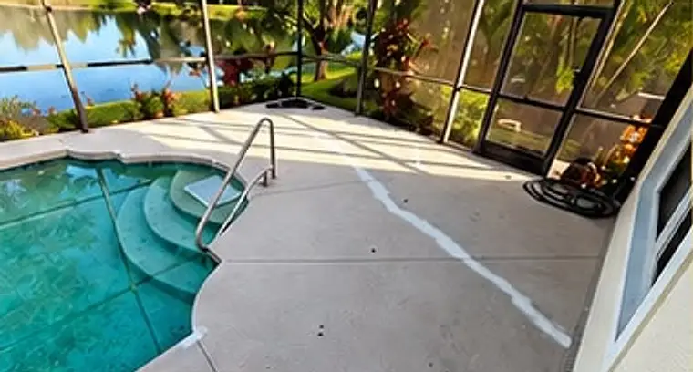 Before: worn concrete pool deck with patched cracks beside the pool steps, inside a screened enclosure