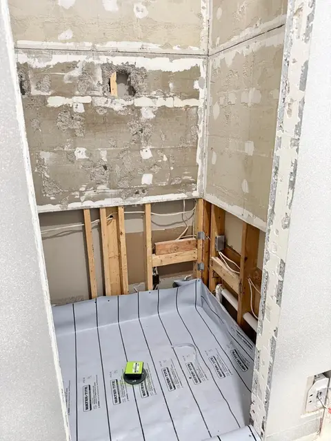Before: shower stripped to bare studs and backer board, with a gray waterproofing membrane on the shower floor